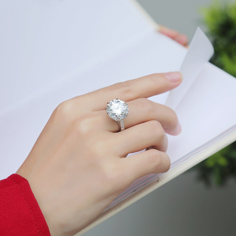 10 karátos moissanite gyűrű kézen viselve, fehér könyv mellett